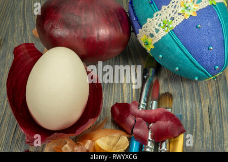 Fresh egg balancing in a dried onion skin, painting brushes and dried onion skin on a wooden table. Easter eggs dyed with onion skins conceptual image Stock Photo