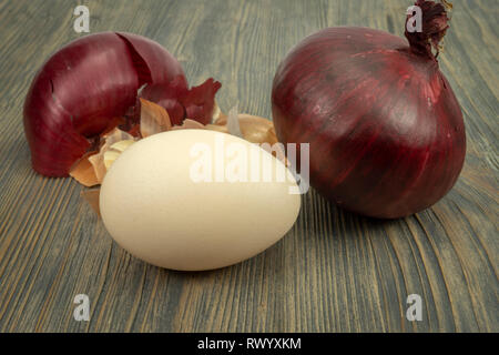 Fresh whole red onion, egg and dried onion skin on a wooden table. Making Easter eggs dyed with onion skins concept Stock Photo