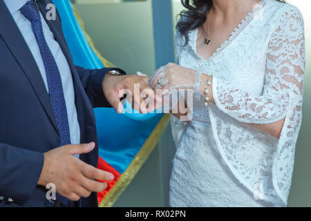 Traditional wedding ceremony at church. The priest is putting golden ring on groom's finger. Happy wedding couple on their celebration. Stock Photo
