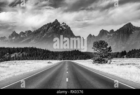 Black and white, country road in front of rugged mountains with cloudy skies, Grand Teton Range, Grand Teton National Park Stock Photo
