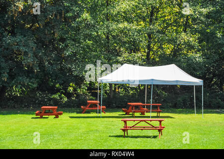 Rest area with red picnic tables and white tent on green lawn in a park Stock Photo