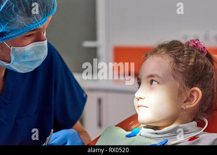 Male dentist examining little girl's teeth. Bright light glowing into the mouth Stock Photo