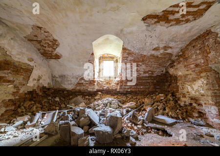 Old forsaken empty basement room of ancient building or palace with cracked plastered brick walls, low arched ceiling, small windows with iron bars an Stock Photo