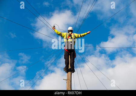 Telecom engineer working on domestic phone line / broadband internet copper wire up a telephone / telegraph pole in a London Street / Road, & blue sky