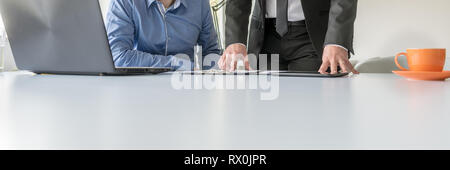 Wide view image of two business man working together at their office desk using laptop computer and reviewing written report. Stock Photo