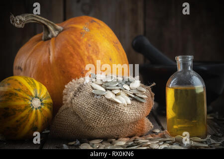 Pumpkin seeds oil bottle, two pumpkins, bag of seeds and mortar on background. Stock Photo