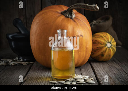 Pumpkin seeds oil bottle closeup, two pumpkins, bag of seeds and mortar on background. Stock Photo