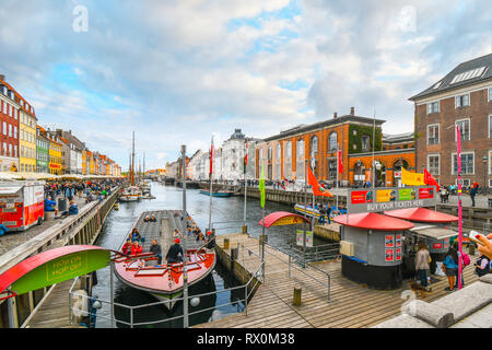 Tourists sightsee, board guide boats and dine at sidewalk cafes on an autumn day on the 17th century waterfront canal Nyhavn in Copenhagen, Denmark. Stock Photo