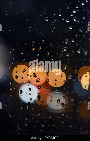 Macro shot of raindrops on window glass during the rain at night in the city. Colorful bokeh in the background Stock Photo