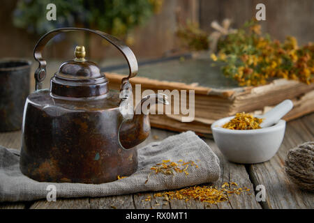 Vintage teapot, mortar of healthy medicinal herbs, old book and Hypericum - St Johns wort bunch. Stock Photo