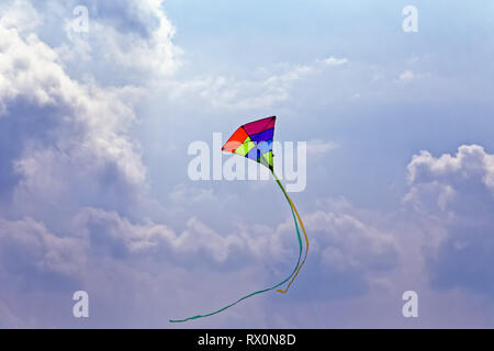 42,518.02980 kite with long curved tail, multi-color multi colored red yellow green blue purple triangular kite flying in sunny cloudy blue sky clouds Stock Photo