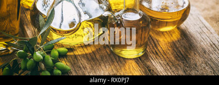 Olive oil in glass bottles and a green fresh olives twig on wooden table, banner, closeup view Stock Photo