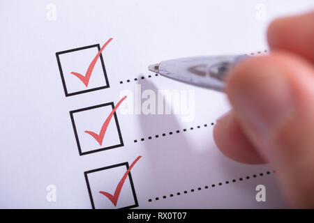 Close-up Of Person's Hand Marking On Checklist With Pen Stock Photo