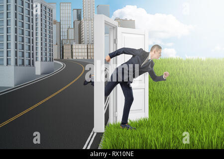 Side view of businessman running from modern city to green field through door standing alone between them with no wall. Stock Photo