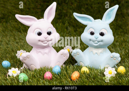 Easter bunnies sitting on grass surrounded by colourful easter eggs Stock Photo