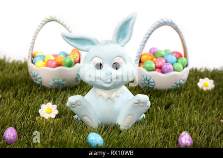 Blue easter bunny sitting in front of easter baskets holding colourful easter eggs on grass. Stock Photo