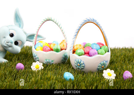 Blue easter bunny peeping into scene of two easter baskets full of colourful eggs on grass with white background Stock Photo