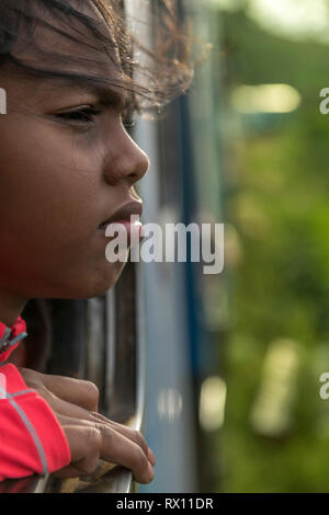 Girl on a train - On a hot day in  March, a young girl enjoys the breeze from the open window on the train journey from Nanu Oya Station to Ella in Sr Stock Photo