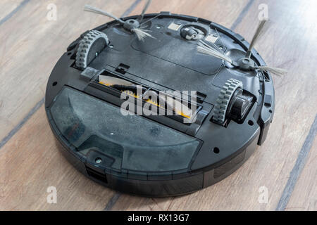 Robot vacuum cleaner upside down on the floor. Covered with dust after cleaning. Stock Photo