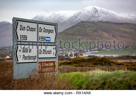 Snow on the mountains in the Irish-speaking area of West Kerry as a sign shows the way to the villages in the area. Stock Photo