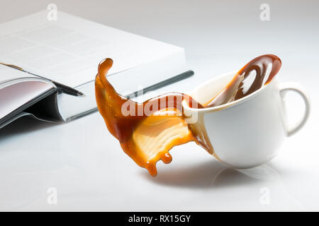 Falling and spilling of a cup of coffee on top of a desk with an open book Stock Photo