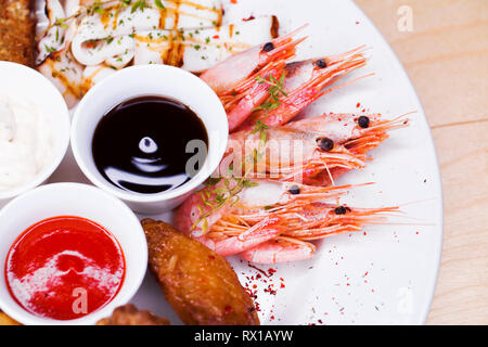 Restaurant dish. Plate of assorted beer snacks, lard, boiled shrimps, fried chicken wings, cheese nuggets and fried black bread Stock Photo