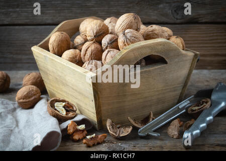 Walnuts in a wooden crate and nutcracker on wooden table. Stock Photo