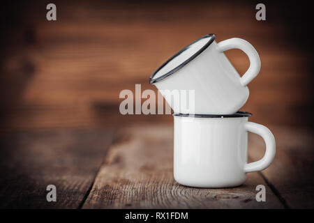 Two enameled cups on wooden rustic kitchen table. Stock Photo