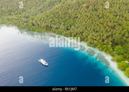 A small dive boat is anchored off the coast of Papua New Guinea. This tropical area is part of the Coral Triangle due to its high marine biodiversity. Stock Photo