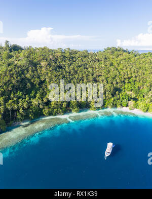 A small dive boat is anchored off the coast of Papua New Guinea. This tropical area is part of the Coral Triangle due to its high marine biodiversity. Stock Photo