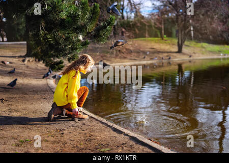 Happy child girl in bright yellow sweater paying with water in a park Stock Photo