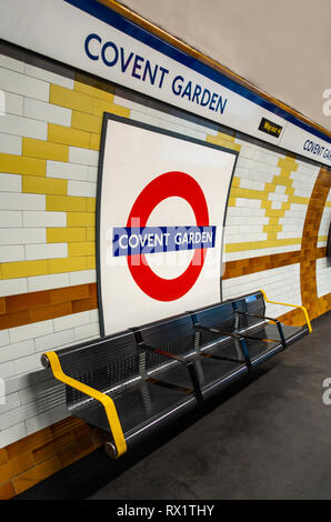 Iconic circular London Tube sign above a public Seat on the underground platform at Covent Garden, London Stock Photo