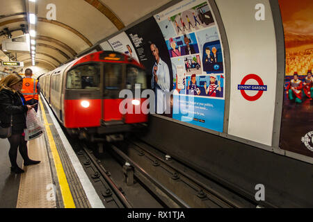 Female Commuter waits for the approaching tube train on a london underground station with ad poster on wall Stock Photo