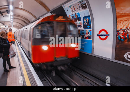 Female Commuter waits for the approaching tube train on london underground track passing ad poster Stock Photo