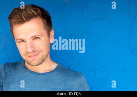 Handsome sunburnt man smiling against blue background and looking at camera Stock Photo