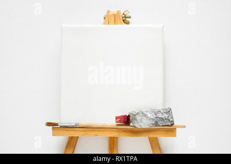 Canvas on easel, paint tube and  paintbrush. White canvas background. Top view. Flat lay. Copy space for text. Stock Photo