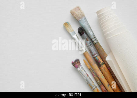 Paintbrushes and roll of artist canvas on white canvas background. Top view. Copy space for text. Stock Photo