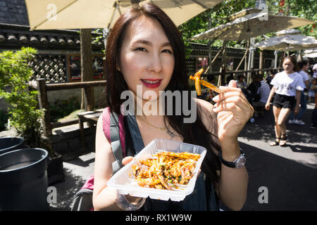 Portrait of smiling woman eating fast food while standing on city street Stock Photo