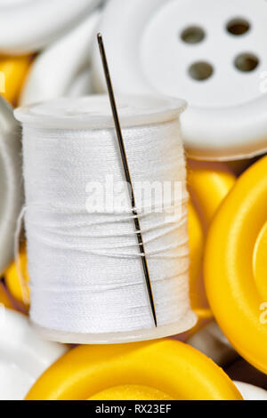 Close up of a spool of white thread with a sewing needle sitting on yellow and white buttons Stock Photo