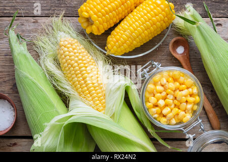Canned sweet corn in glass jar, fresh and cooked corn on cobs, salt. Top view. Stock Photo