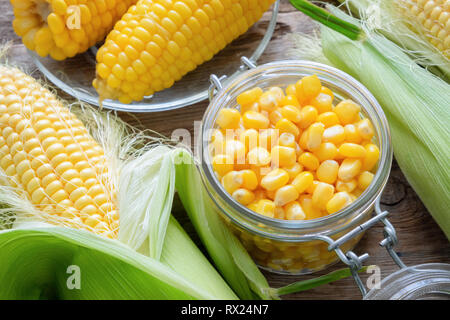 Canned sweet corn in glass jar, fresh and cooked corn on cobs. Top view. Stock Photo