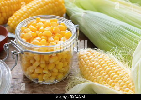 Canned sweet corn in glass jar, fresh and cooked corn on cobs. Stock Photo