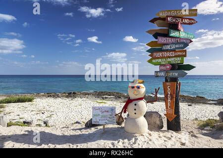 Post Sign with directions to World travel destinations and Isolated Christmas Snowman on Sandy Beach Punta Sur Ecological Reserve in Cozumel, Mexico Stock Photo