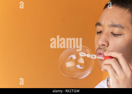Young adult man blowing soap bubbles on orange background. Stock Photo