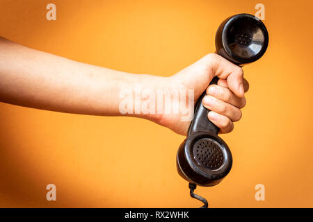 Hand holding old telephone receiver on orange background. Stock Photo