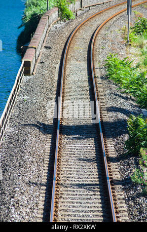 Old railroad tracks run along the blue lake in the green mountains Stock Photo