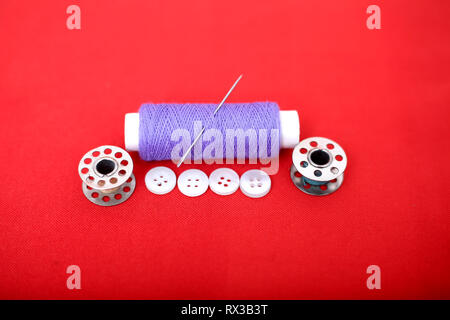 Picture of spool thread, needle, bobbin and button. Isolated on the red background. Stock Photo