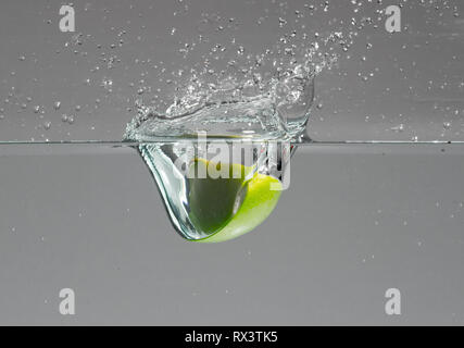 Green apple slice falls into water and creates beautiful air bubbles and water splashes Stock Photo