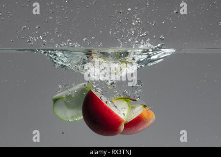 Red and green apple slices fall into water and create beautiful air bubbles and water splashes Stock Photo