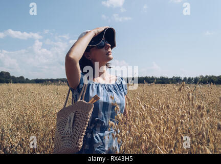 profile of beautiful woman in sunglasses and hat looking at the sun in oat field Stock Photo